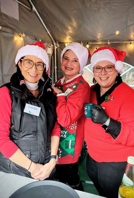 Drei Frauen mit Weihnachtsmützen stehen in einem Zelt