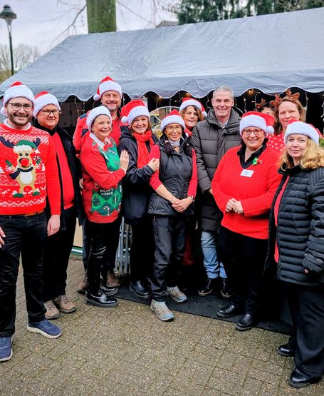 Menschen mit Weihnachtsmützen, roten Oberteilen und schwarzen Hosen stehen vor einem Stand