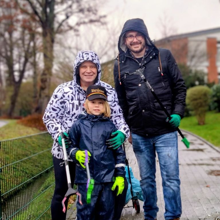 Eine Frau, ein Kind, ein Mann mit Müllgreifzangen.