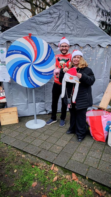 Zwei Menschen mit Weihnachtsmützen stehen neben einem Glücksrad