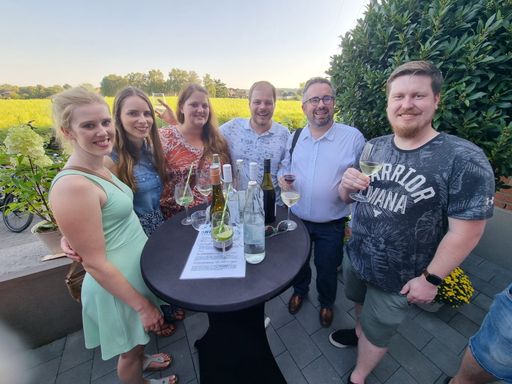 Menschen stehen an einem Stehtisch mit Weingläsern und lächeln