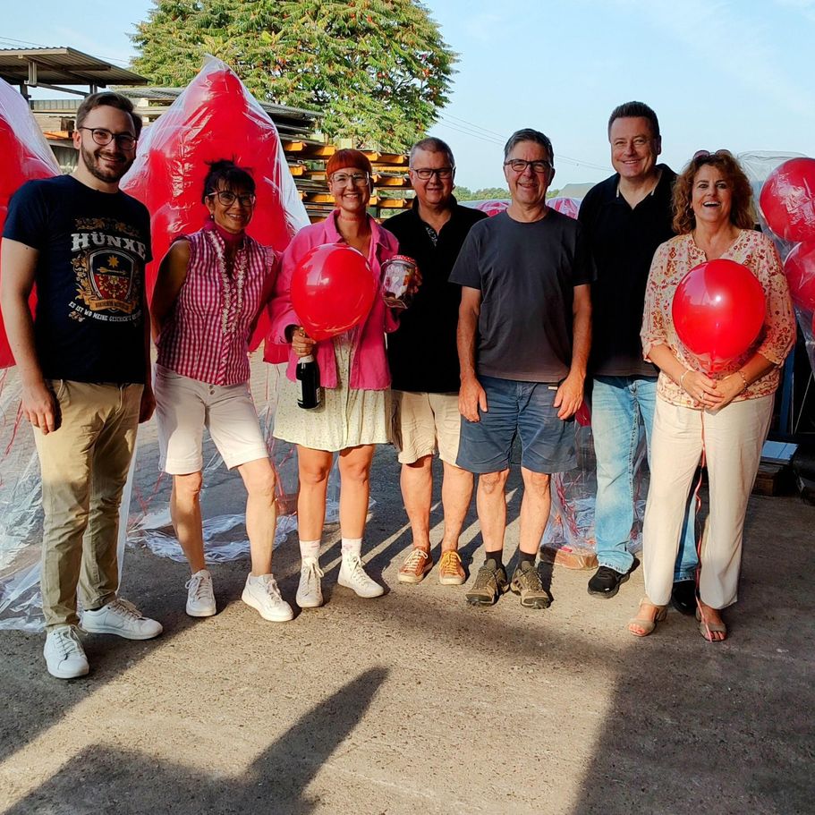 Menschen stehen zusammen. Zwei Menschen halten einen roten Luftballon
