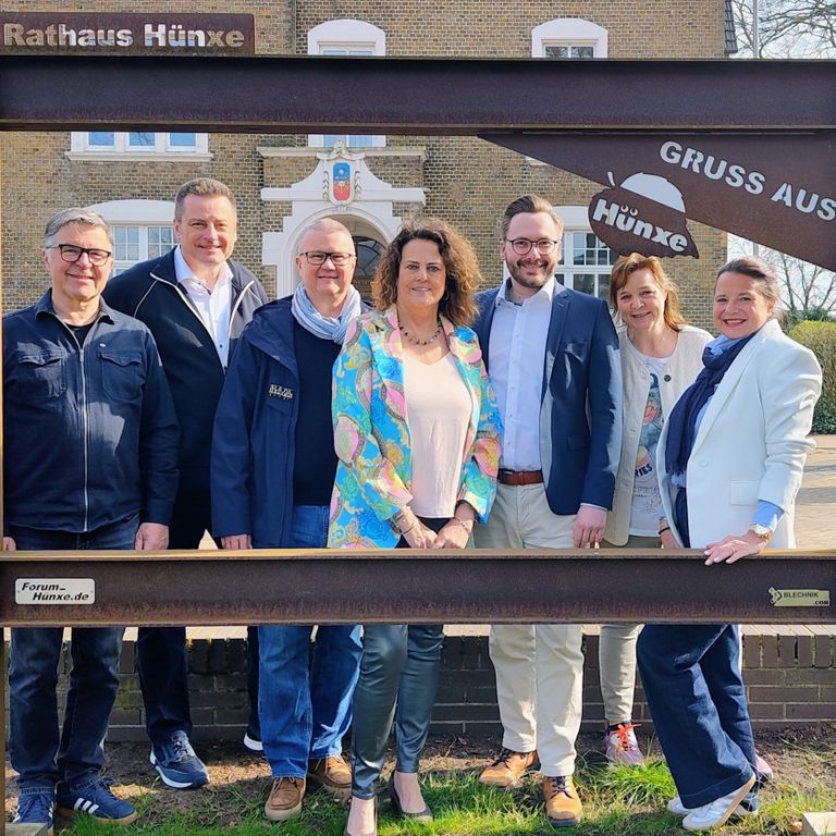 Menschen stehen in einem Rahmen vor einem Rathaus.